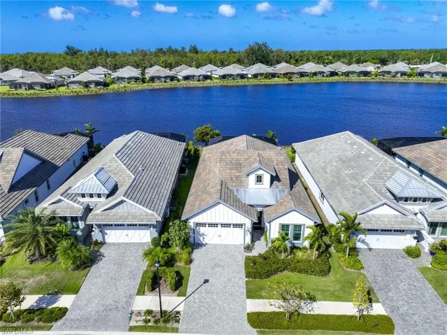 Aerial perspective of a waterfront residential property featuring a paver driveway, multi-gabled roofline, metal roof accents, and vertical board-and-batten siding
