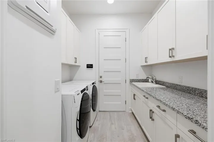 Laundry room featuring white cabinetry, stone-finish countertops, an undermount sink, and wood-finish flooring