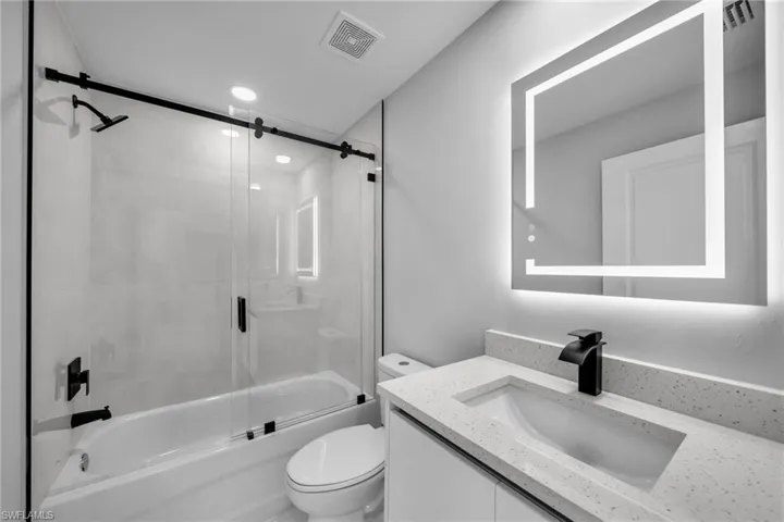 Full bathroom featuring vanity, enclosed tub / shower combo, and toilet