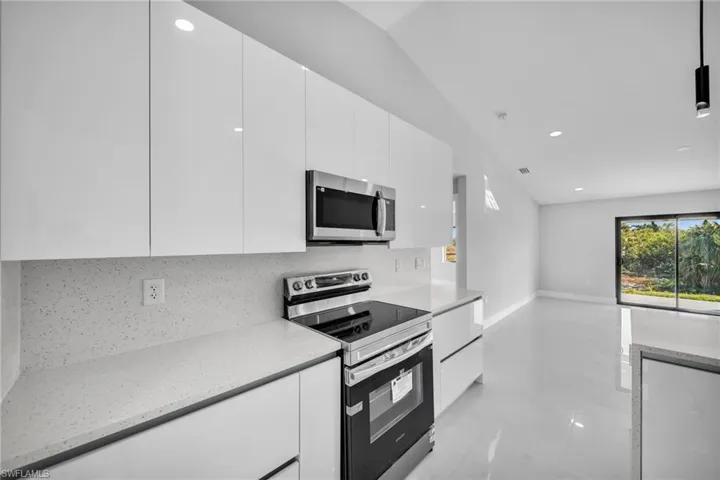 Kitchen with decorative backsplash, light stone countertops, white cabinets, and appliances with stainless steel finishes