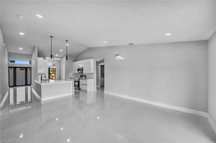 Kitchen with lofted ceiling, white cabinetry, a center island with sink, appliances with stainless steel finishes, and pendant lighting