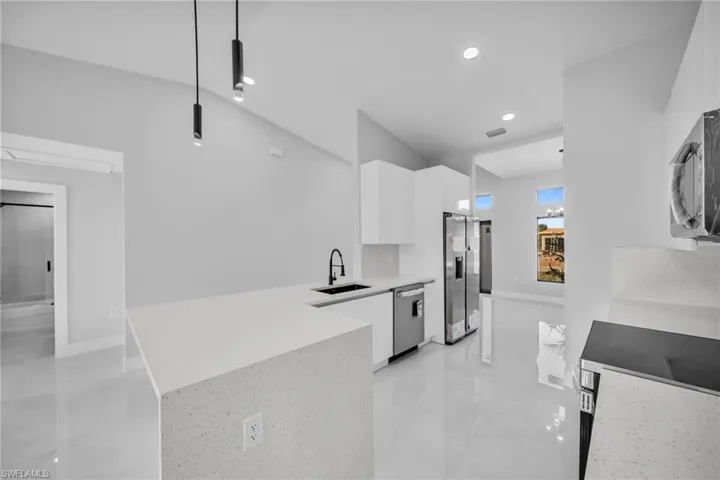 Kitchen featuring sink, decorative light fixtures, appliances with stainless steel finishes, kitchen peninsula, and white cabinets