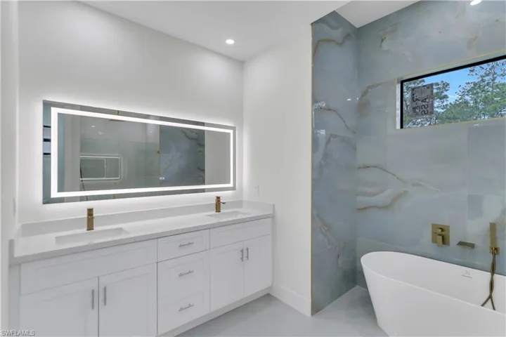 Bathroom with a freestanding bath, double vanity, a sink, and recessed lighting