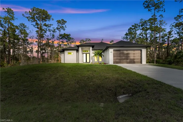 View of front of property with a garage, concrete driveway, and a lawn