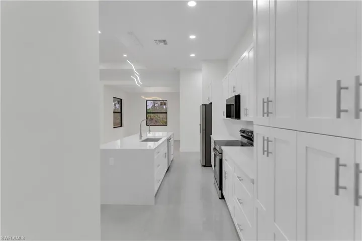 Kitchen featuring a center island with sink, visible vents, appliances with stainless steel finishes, white cabinetry, and a sink