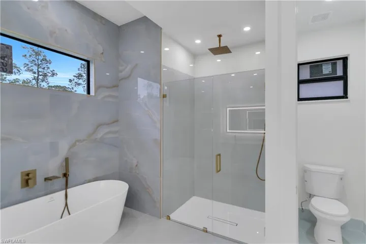 Full bathroom with visible vents, toilet, a soaking tub, a shower stall, and tile walls