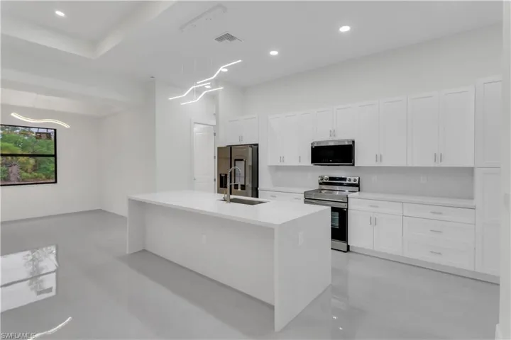 Kitchen with appliances with stainless steel finishes, a kitchen island with sink, light countertops, white cabinetry, and a sink