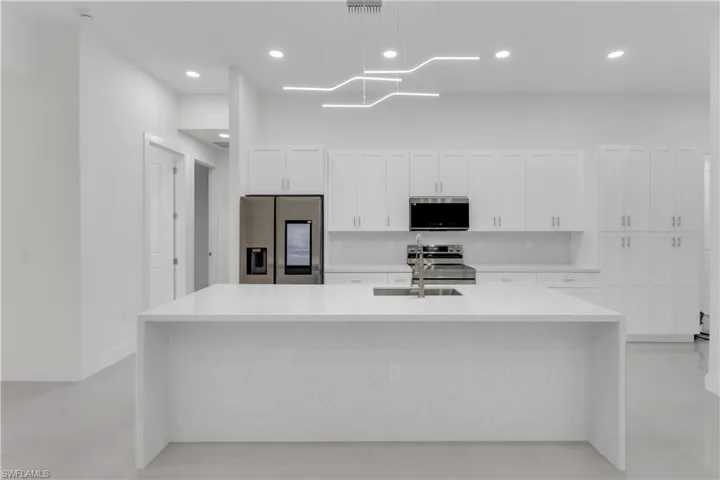 Kitchen featuring visible vents, white cabinets, an island with sink, stainless steel appliances, and a sink