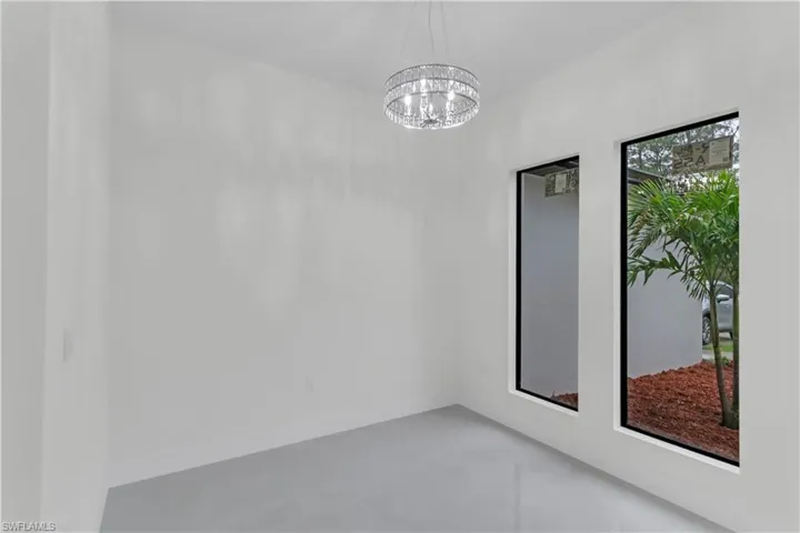 Spare room with finished concrete flooring, a chandelier, and baseboards