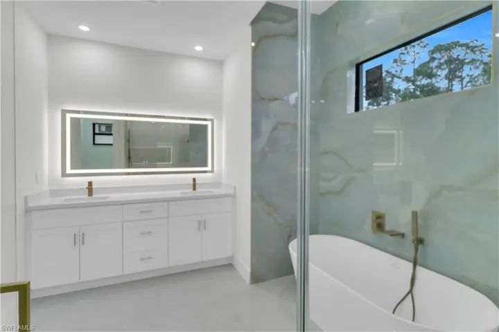 Bathroom featuring double vanity, a soaking tub, a sink, and recessed lighting