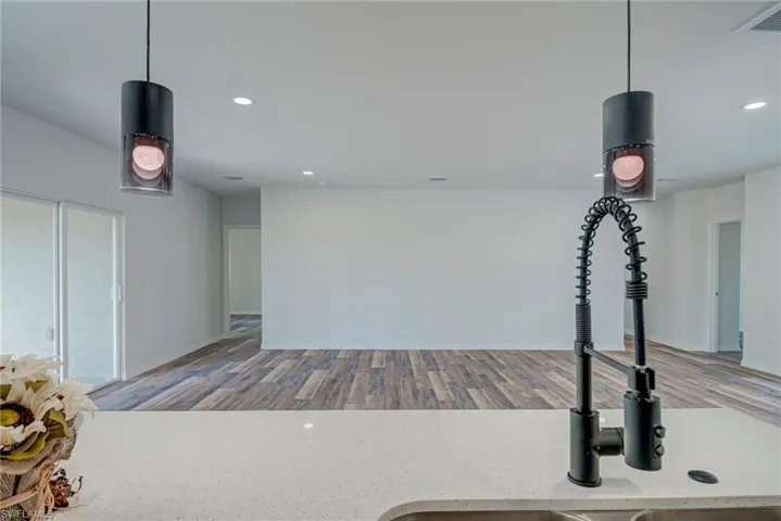 Kitchen view of pendant lighting, light stone countertops, recessed lighting, and wood finished floors