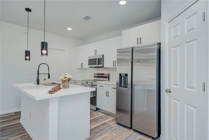 Kitchen featuring stainless steel appliances, decorative light fixtures, light wood-type flooring, white cabinetry, and a center island with sink