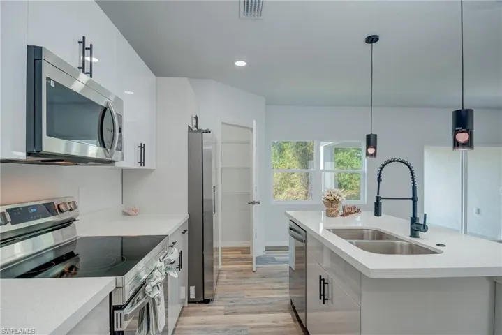 Kitchen featuring stainless steel appliances, modern cabinets, light wood finished floors, decorative light fixtures, and white cabinets