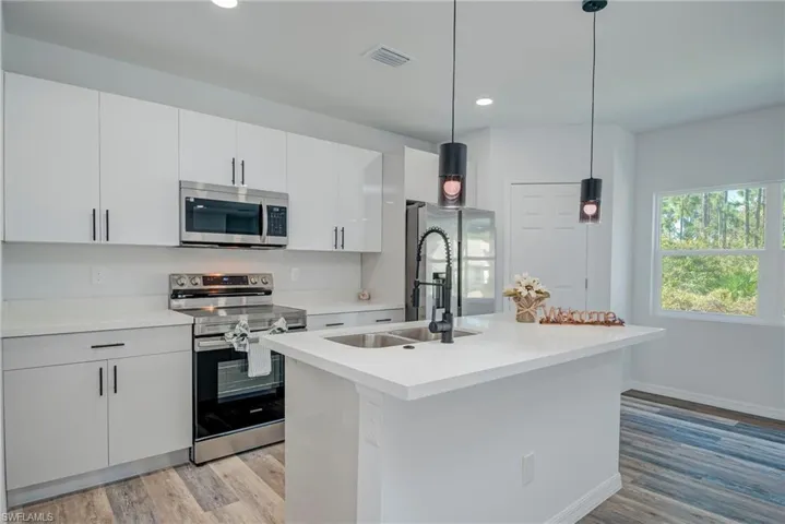 Kitchen with stainless steel appliances, pendant lighting, a center island with sink, light wood-style flooring, and white cabinetry