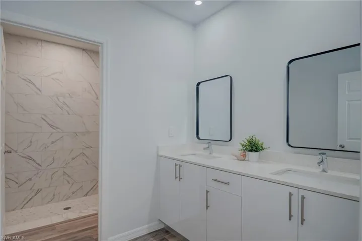 Full bathroom featuring double vanity, a walk in shower, and light wood-type flooring