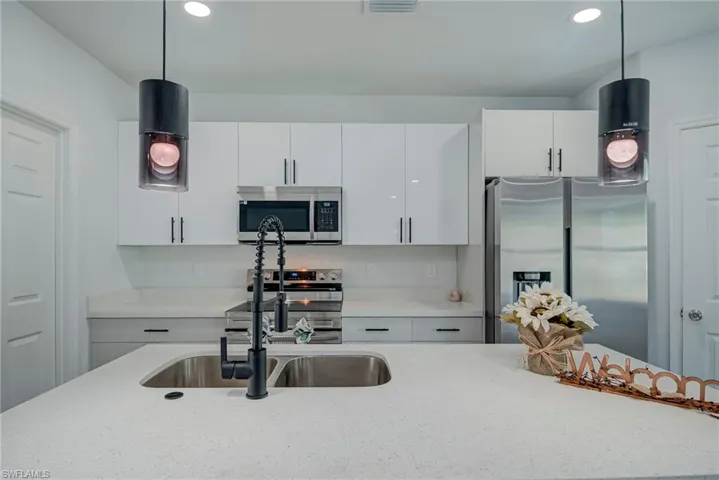 Kitchen featuring hanging light fixtures, light stone countertops, appliances with stainless steel finishes, white cabinetry, and recessed lighting