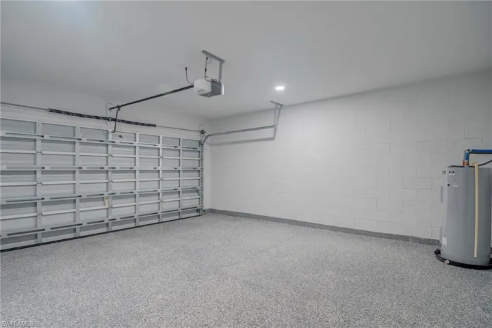 Garage featuring electric water heater, concrete block wall, recessed lighting, and a garage door opener