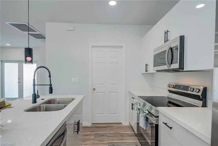 Kitchen with appliances with stainless steel finishes, recessed lighting, white cabinetry, light stone counters, and light wood-type flooring
