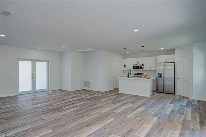 Kitchen with open floor plan, decorative light fixtures, appliances with stainless steel finishes, an island with sink, and white cabinets