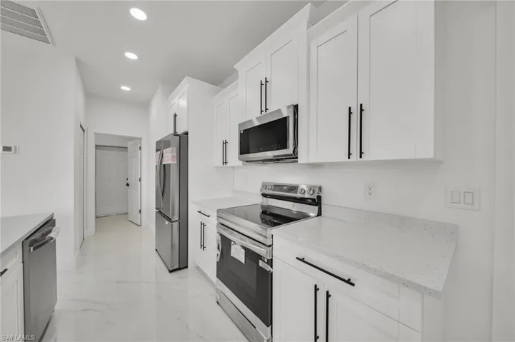 Kitchen with appliances with stainless steel finishes, light marble finish flooring, white cabinetry, recessed lighting, and light stone counters