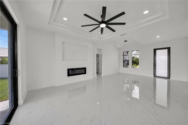 Unfurnished living room with a raised ceiling, recessed lighting, a glass covered fireplace, light marble finish flooring, and ceiling fan