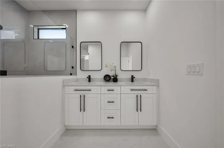 Bathroom with a marble finish shower, light marble finish floors, and double vanity