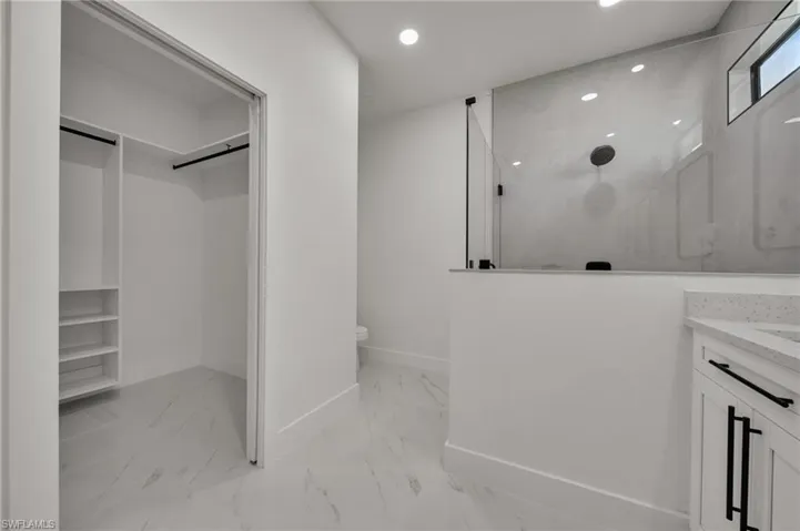 Bathroom featuring a spacious closet, a marble finish shower, vanity, light marble finish flooring, and recessed lighting