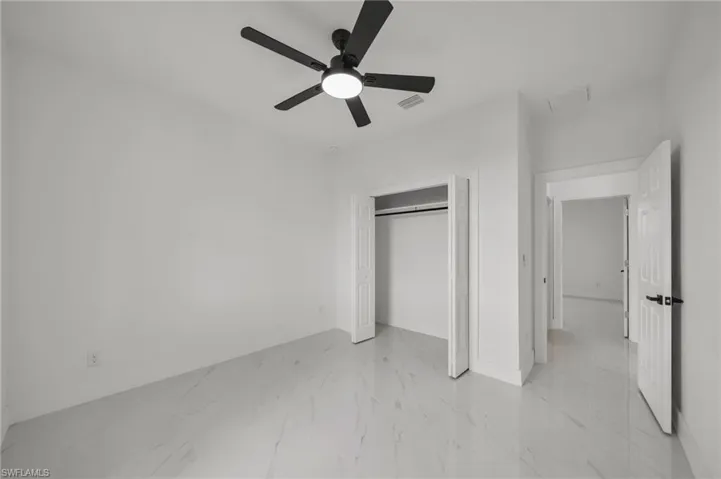 Unfurnished bedroom featuring a closet, light marble finish flooring, and a ceiling fan