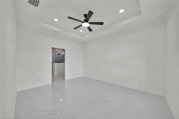 Unfurnished room with a tray ceiling, light marble finish flooring, recessed lighting, and ceiling fan