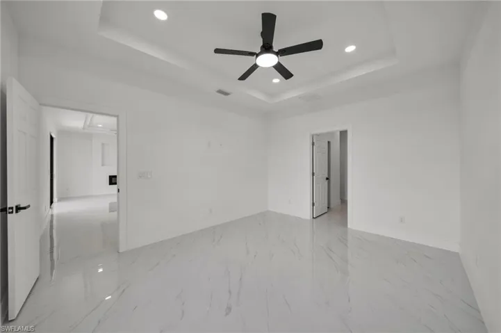 Empty room featuring a tray ceiling, attic access, recessed lighting, light marble finish flooring, and a ceiling fan