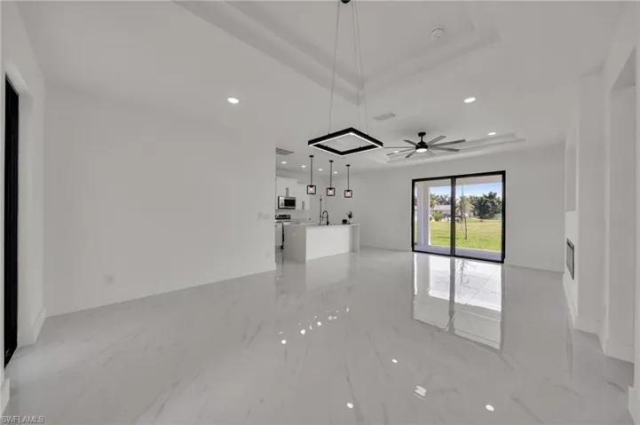 Unfurnished living room featuring a tray ceiling, recessed lighting, light marble finish flooring, and a ceiling fan