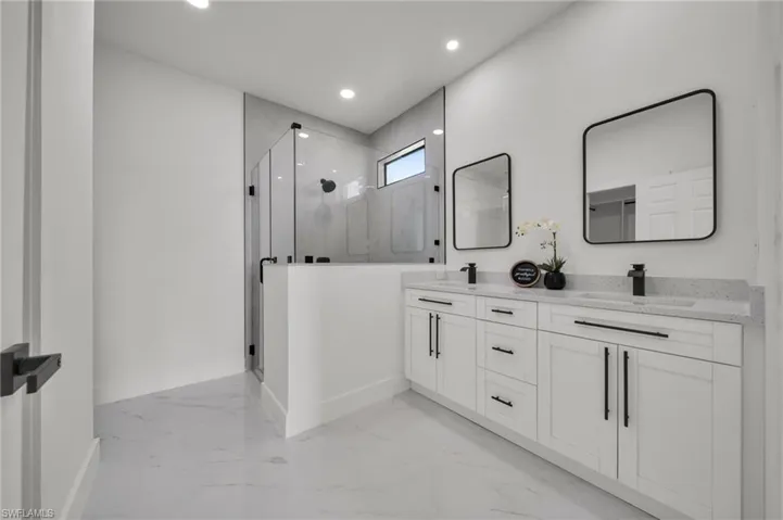 Bathroom with a marble finish shower, double vanity, light marble finish floors, and recessed lighting