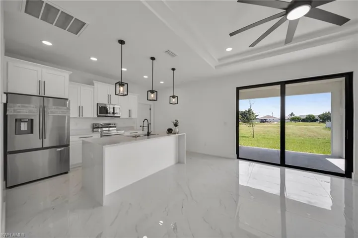 Kitchen featuring appliances with stainless steel finishes, pendant lighting, an island with sink, white cabinetry, and light marble finish floors