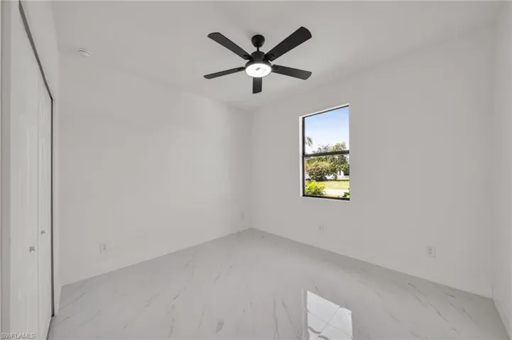 Unfurnished bedroom with marble look tiles, ceiling fan, and a closet