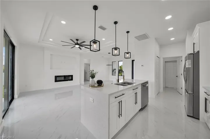 Kitchen featuring light marble finish flooring, white cabinetry, light stone countertops, an island with sink, and recessed lighting