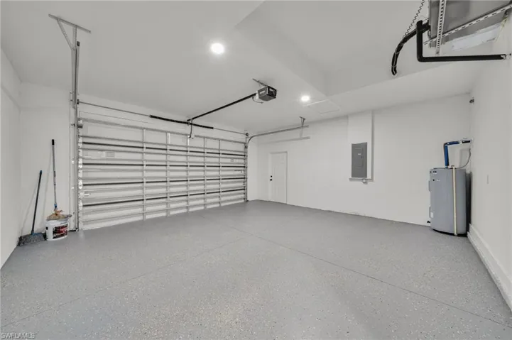 Garage featuring electric panel, recessed lighting, a garage door opener, and water heater