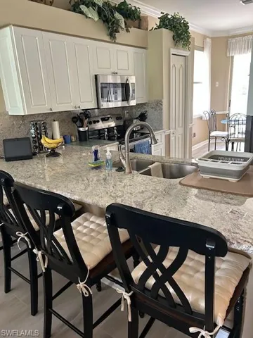 Kitchen featuring decorative backsplash, ornamental molding, stainless steel appliances, a sink, and a breakfast bar area