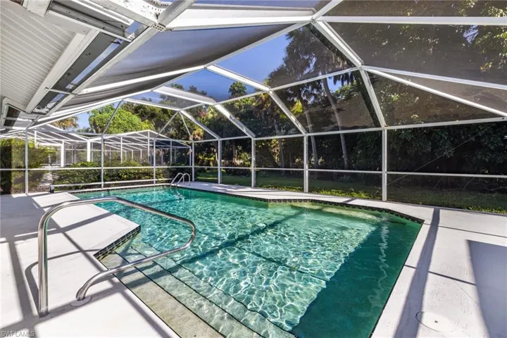 Screened pool enclosure featuring a rectangular swimming pool with integrated steps, a handrail, and surrounding concrete decking