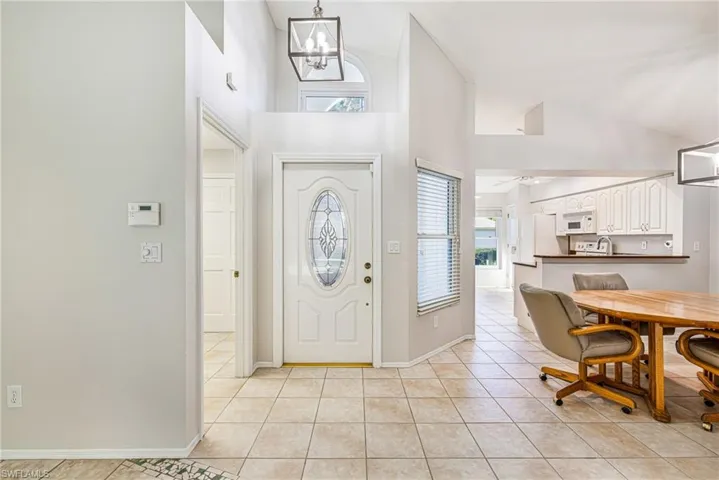 Tiled entryway with a decorative glass front door, vaulted ceilings, and a contemporary pendant light fixture