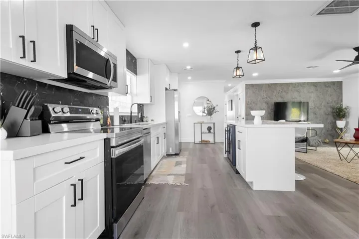 Kitchen featuring ceiling fan, hardwood / wood-style floors, decorative light fixtures, white cabinets, and appliances with stainless steel finishes