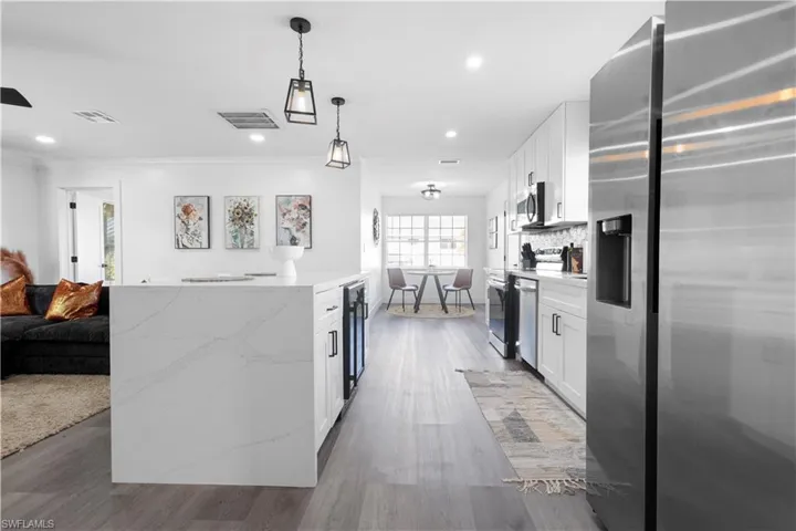 Kitchen with light stone countertops, pendant lighting, wood-type flooring, white cabinets, and appliances with stainless steel finishes