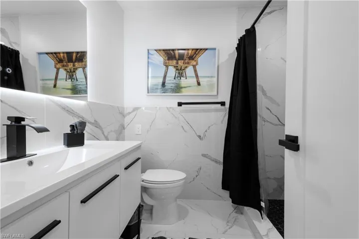 Bathroom with tile walls, a shower with curtain, tasteful backsplash, toilet, and large vanity