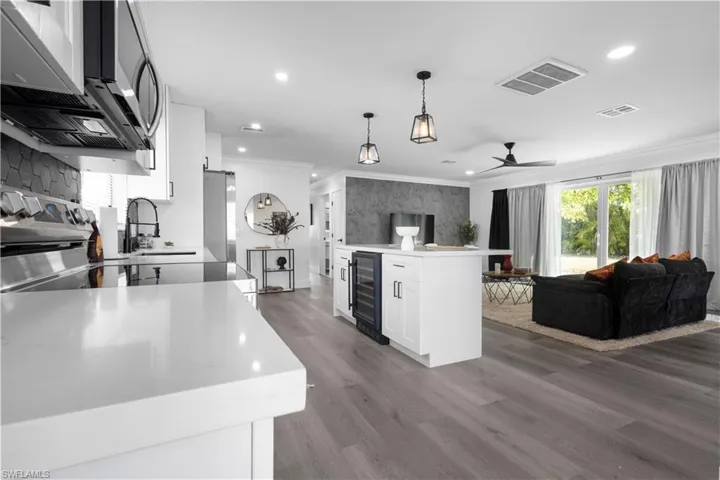 Kitchen featuring beverage cooler, decorative light fixtures, wood-type flooring, white cabinetry, and appliances with stainless steel finishes
