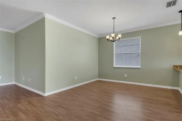 Spare room with ornamental molding, dark wood-style floors, and suspended lighting