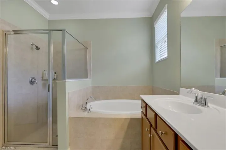 Bathroom featuring vanity, a garden tub, a stall shower, and crown molding