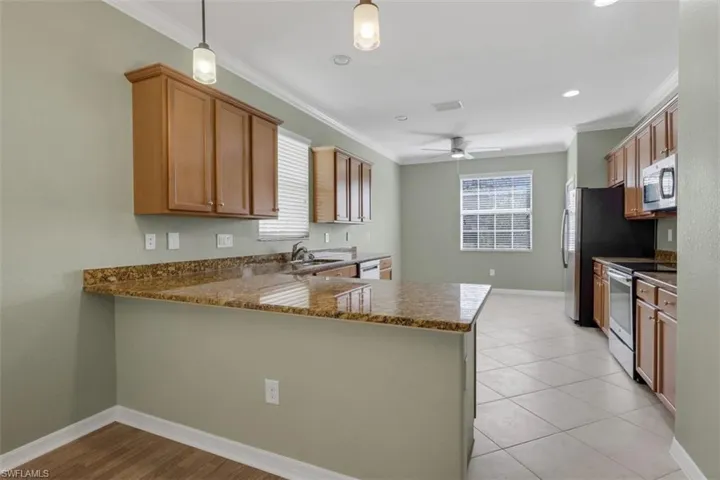 Kitchen featuring a peninsula, stainless steel appliances, wood finish cabinets, dark stone countertops, and ornamental molding