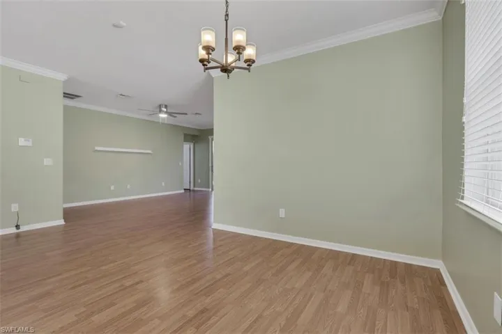 Spare room with crown molding, hanging lights, light wood-style floors, and ceiling fan