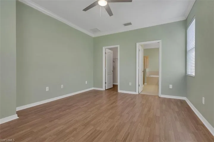 Unfurnished bedroom with a spacious closet, crown molding, light wood-style floors, ceiling fan, and ensuite bath