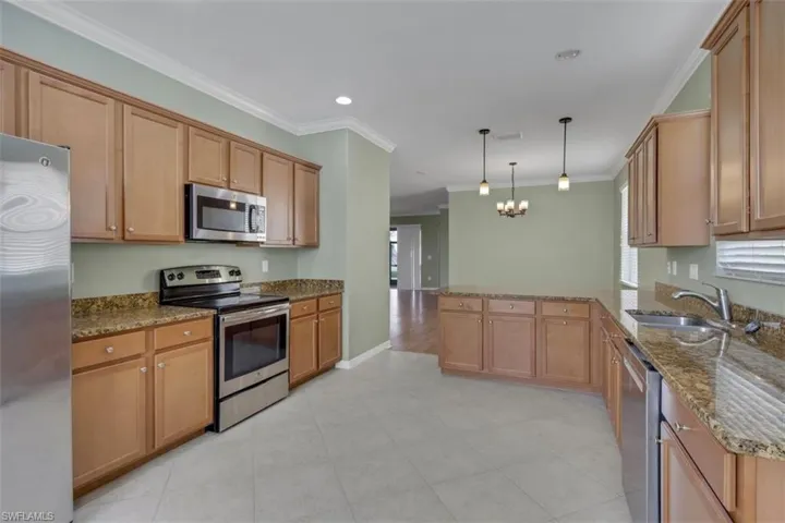 Kitchen with dark stone countertops, stainless steel appliances, a peninsula, crown molding, and suspended lighting
