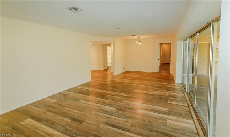 Spacious room featuring wood-finish flooring, light-colored wall paint, recessed lighting, and expansive glass sliding doors